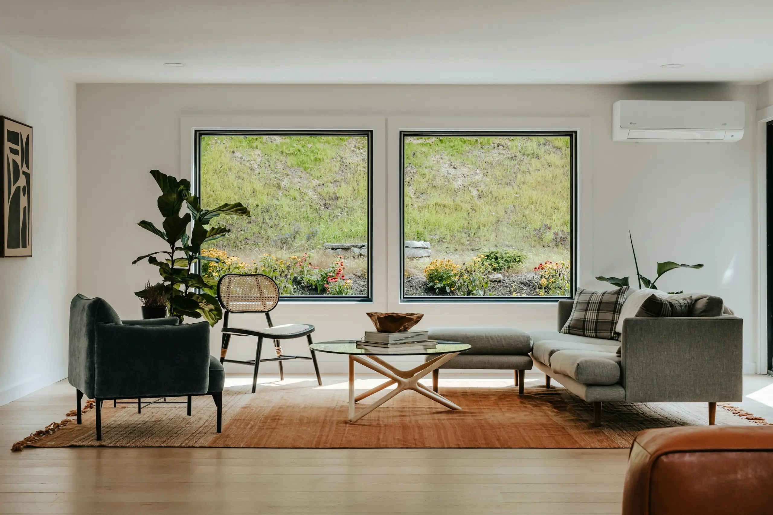 A bright, clean living room with two big windows, a rug, a sofa and armchairs.